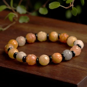 Golden Silk Jade Lotus Bracelet displayed on wooden surface with natural lighting, showing warm gradient beads and carved lotus charm details
