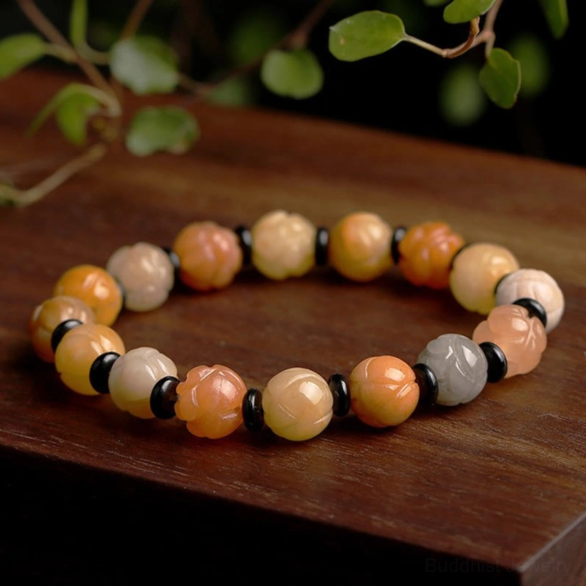 Golden Silk Jade Lotus Bracelet displayed on wooden surface with natural lighting, showing warm gradient beads and carved lotus charm details