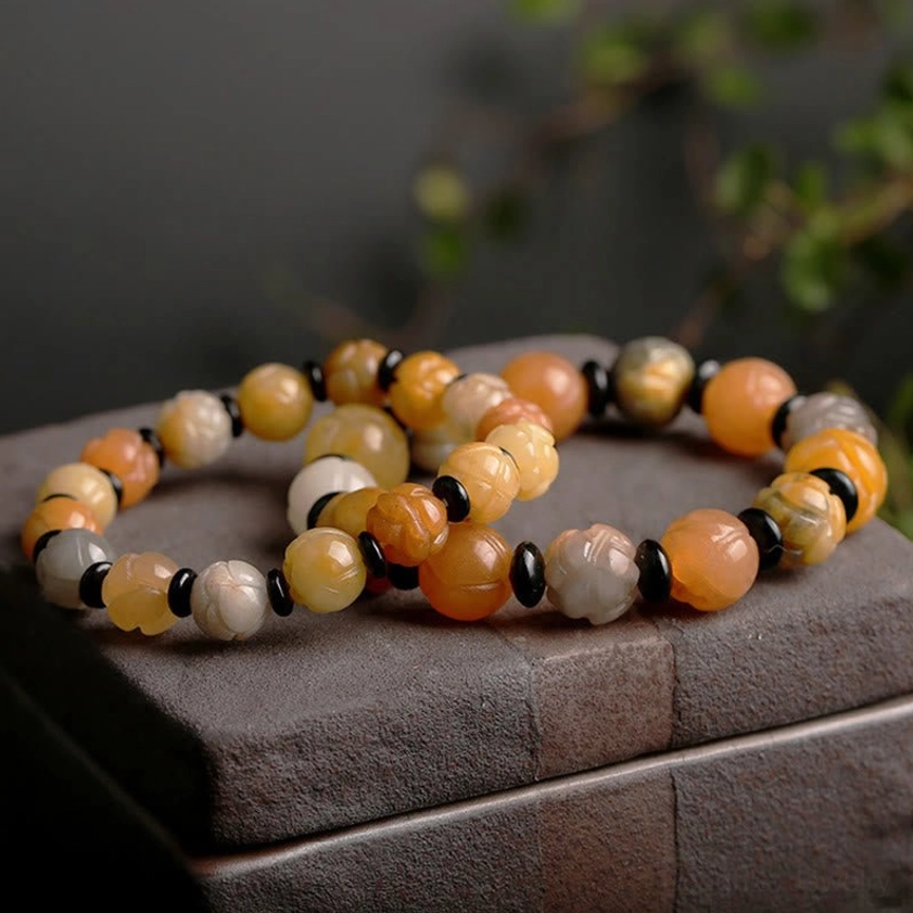 Pair of Golden Silk Jade Lotus Bracelets displayed together on dark stone box with green foliage, showing multiple warm tone variations