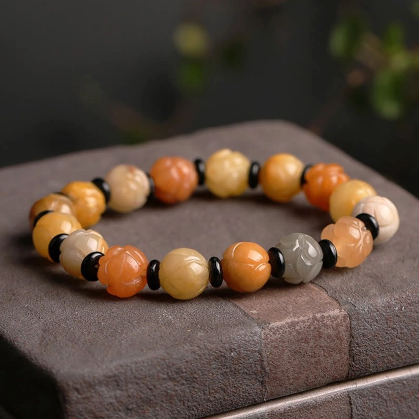 Golden Silk Jade Lotus Bracelet on dark stone pedestal display showing carved lotus charm and warm color gradient
