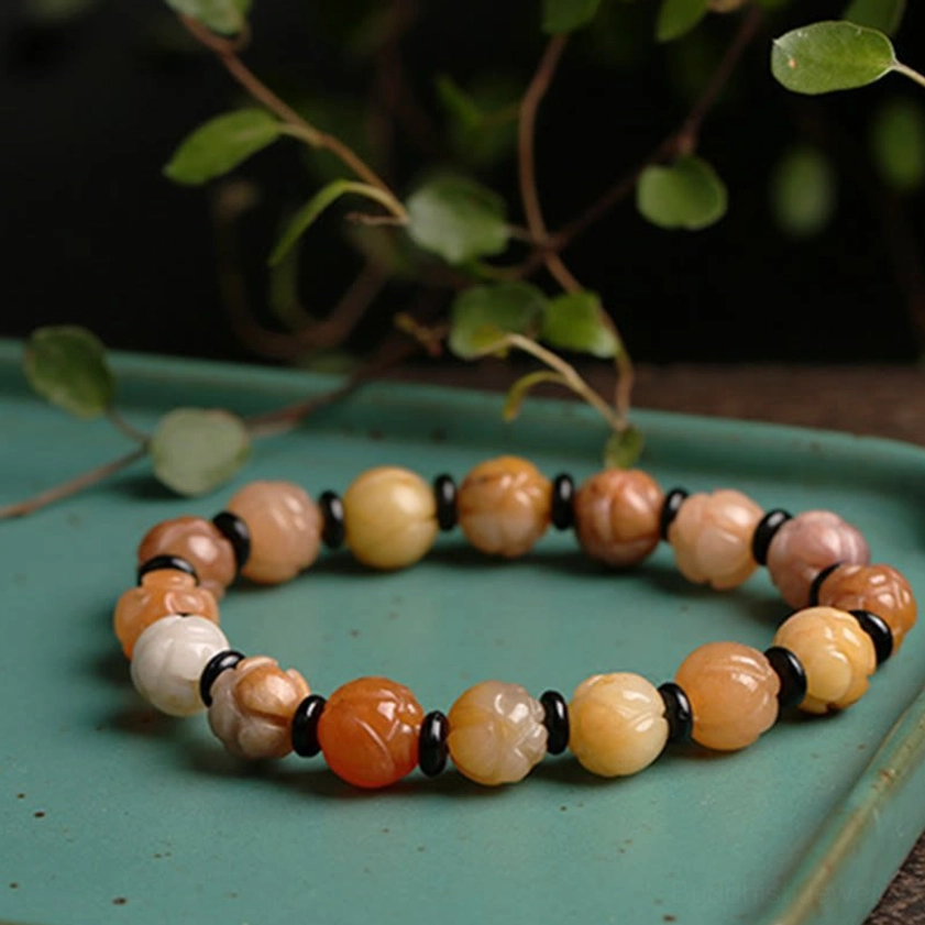 Golden Silk Jade Lotus Bracelet with reddish warm tones displayed on teal tray with botanical background