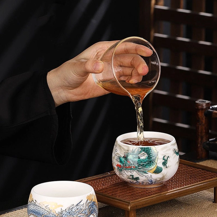 Pouring brewed tea into handcrafted green dragon ceramic cup on wooden tea tray with blue dragon cup beside