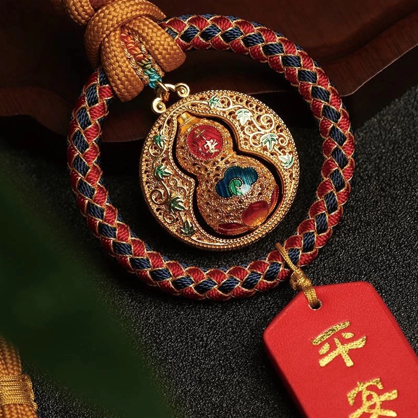 Close-up detail of enamel gourd charm with filigree design, woven rope, and Ping An blessing tag