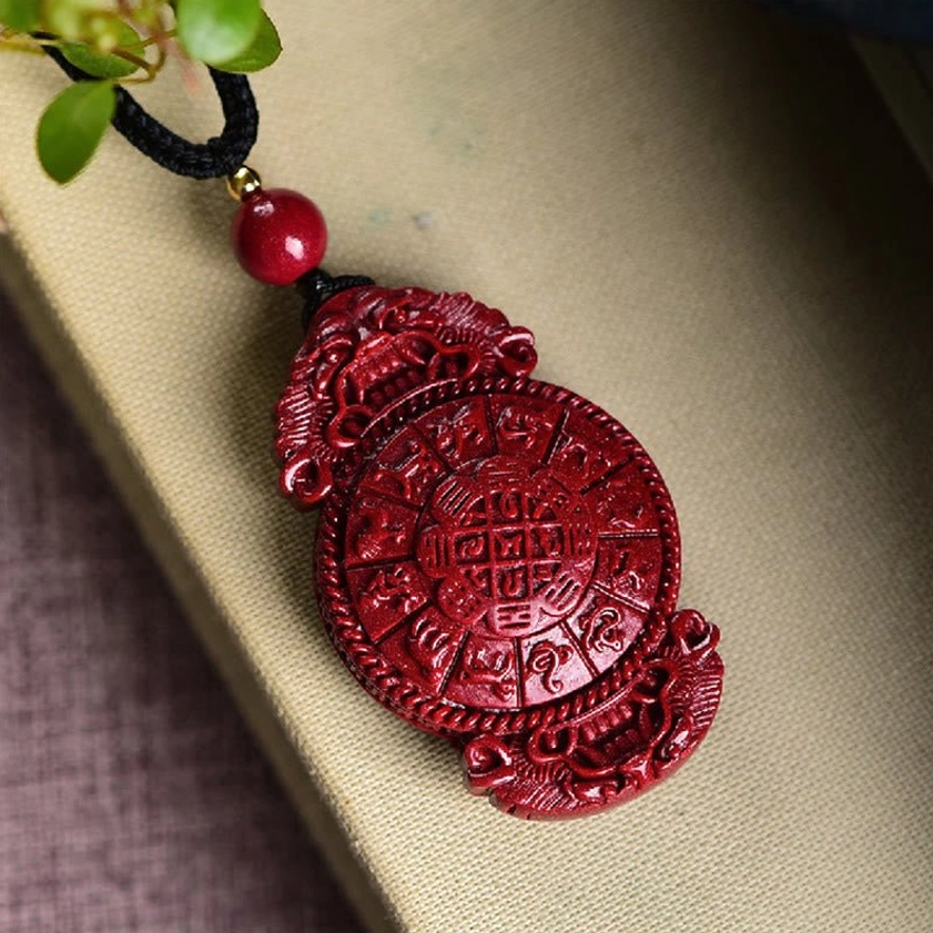 Gourd-shaped cinnabar Buddhist pendant held in hand showing wine-red color and carved details against dark background