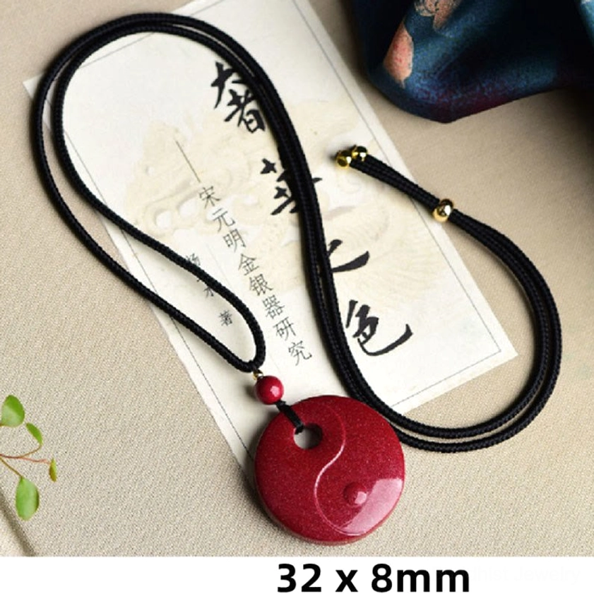 Gourd-shaped cinnabar Buddhist pendant necklace on black cord displayed on tabletop with ceramic containers and green plants