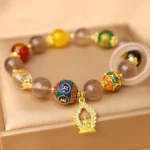 Gray agate Om Mani Padme Hum Buddha charm bracelet with gold accents displayed on luxury satin jewelry tray, featuring enamel mantra beads and crystal accents