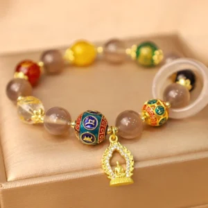 Gray agate Om Mani Padme Hum Buddha charm bracelet with gold accents displayed on luxury satin jewelry tray, featuring enamel mantra beads and crystal accents
