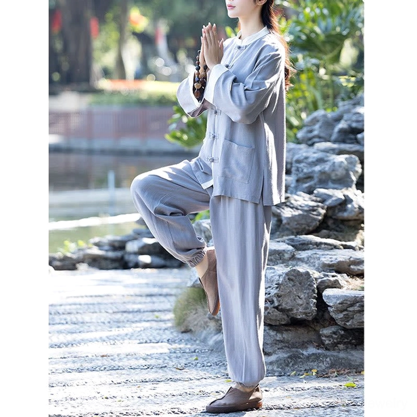 Gray zen wear meditation suit, side full-body view with woman in prayer pose by waterside garden