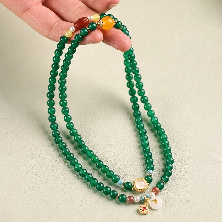 Green agate Buddhist prayer mala held in hand showing texture and full 108-bead count with decorative pendants