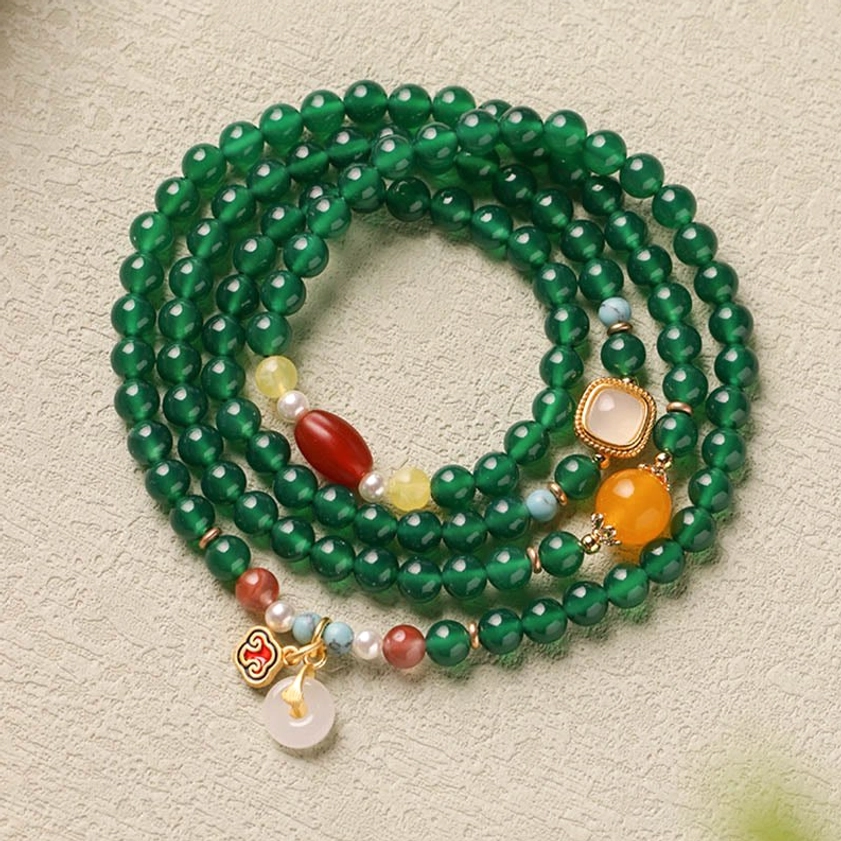 Green agate Buddhist mala bracelet with peace buckle and cloud charm embellishments on textured surface