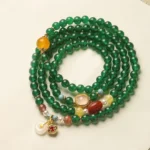 Green agate Buddhist mala bracelet with mixed gemstone charms and peace buckle pendant in flat lay view
