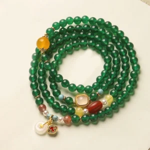 Green agate Buddhist mala bracelet with mixed gemstone charms and peace buckle pendant in flat lay view