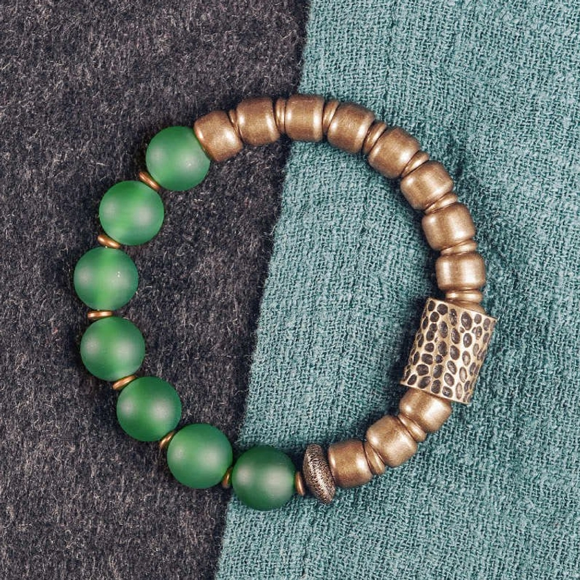 Green agate stone Buddhist bracelet close-up on wrist with teal fabric background showing single bead focus