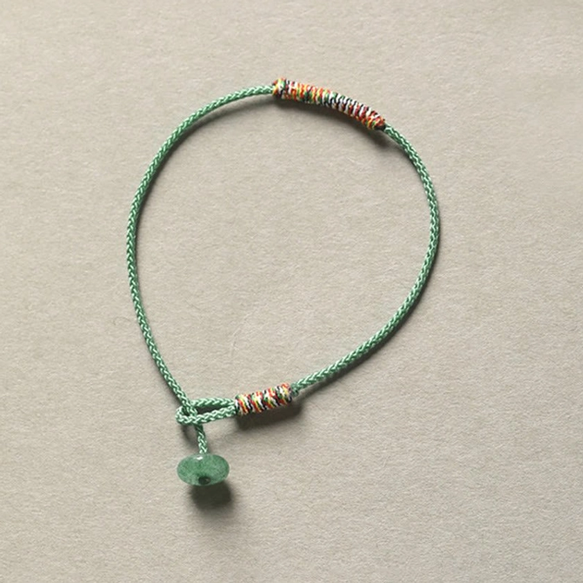 Green aventurine Buddhist bracelet with detailed woven string trim and protective charm, overhead flat lay photography