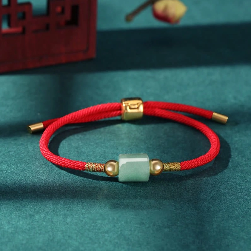 Single adjustable Buddhist green aventurine red string bracelet with gold metal accents and sliding clasp on teal background