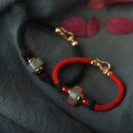 Green aventurine and red agate Buddhist luck bracelet with gold charm, flat lay displaying braided string design and bead details