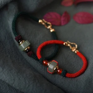 Green aventurine and red agate Buddhist luck bracelet with gold charm, flat lay displaying braided string design and bead details