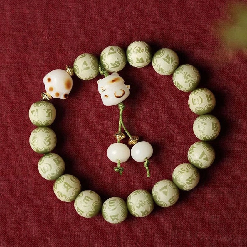 Large green Bodhi seed bracelet with two cat paw pendants and matching bead tassel on red fabric background