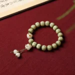 Green Bodhi seed bracelet with engraved Om Mani Padme Hum mantra and white cat paw pendants displayed on dark red fabric