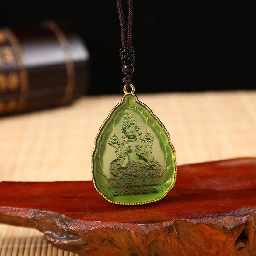 Green Tibetan Tara Buddhist crystal pendant necklace showing embossed Buddha figure with green crystal body and gold border on bamboo mat background