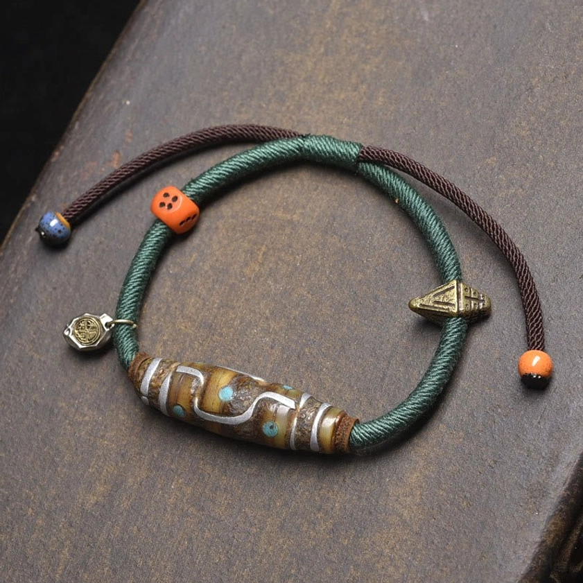 Green and brown braided rope nine-eye dzi bead bracelet with retro metal pendants and decorative beads overhead view