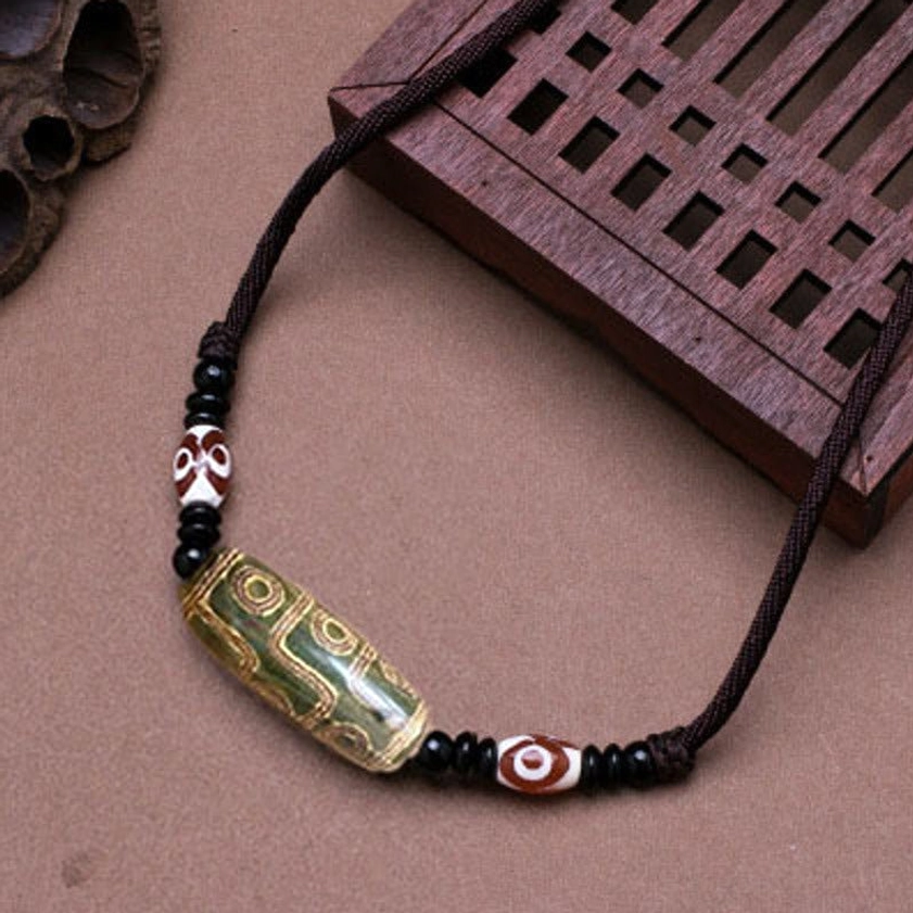 Green vintage Buddhist dzi bead necklace with textured agate stone and black spacer beads, overhead flat lay on wooden surface