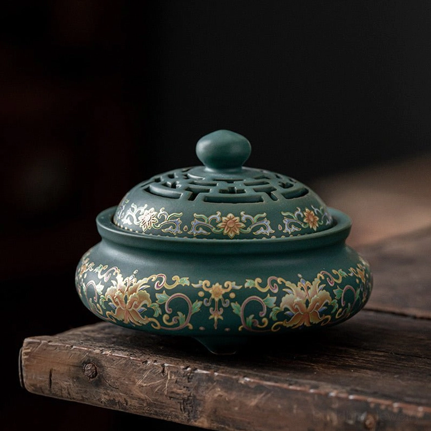 Teal green ceramic incense burner with floral scroll patterns, hollow carved lid, three-footed base, low angle front view