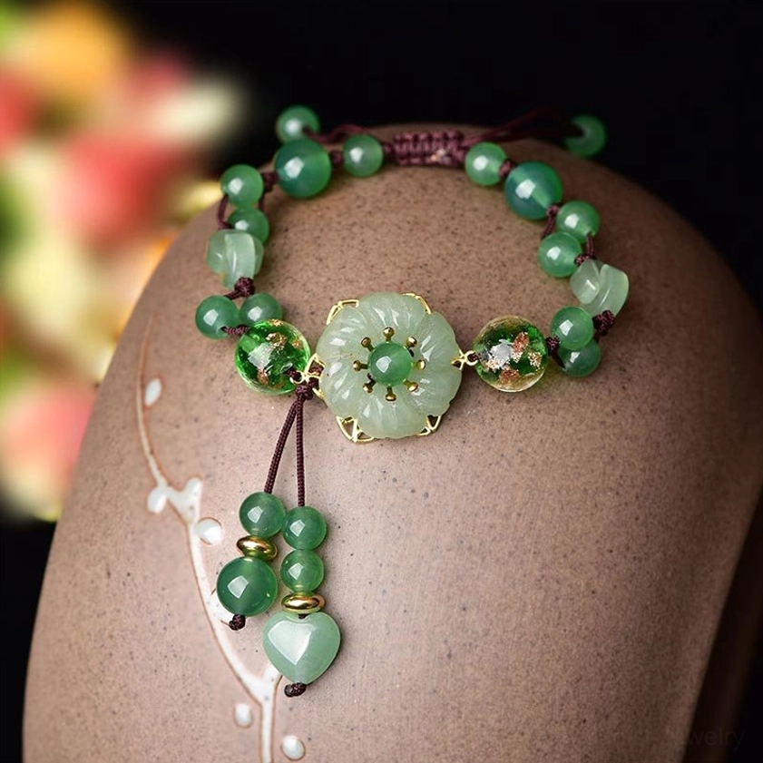 Top-down view of green jade beaded bracelet with gold-trimmed dangling heart jade pendant on ceramic display stand