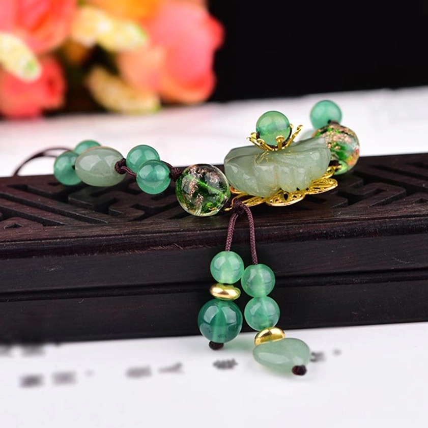 Natural green fancy jade bracelet with large carved jade ornament, gold foil beads, and dangling tassel on black stand with floral background