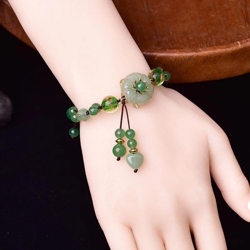 Green jade bracelet worn on wrist showing how the dangling tassel hangs naturally, side view on wooden table