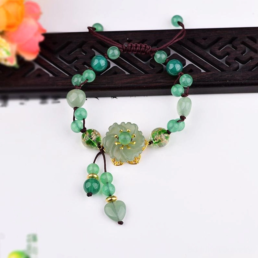 Handmade green jade bracelet with braided cord, jade flower charm, and complete tassel set on black carved display stand