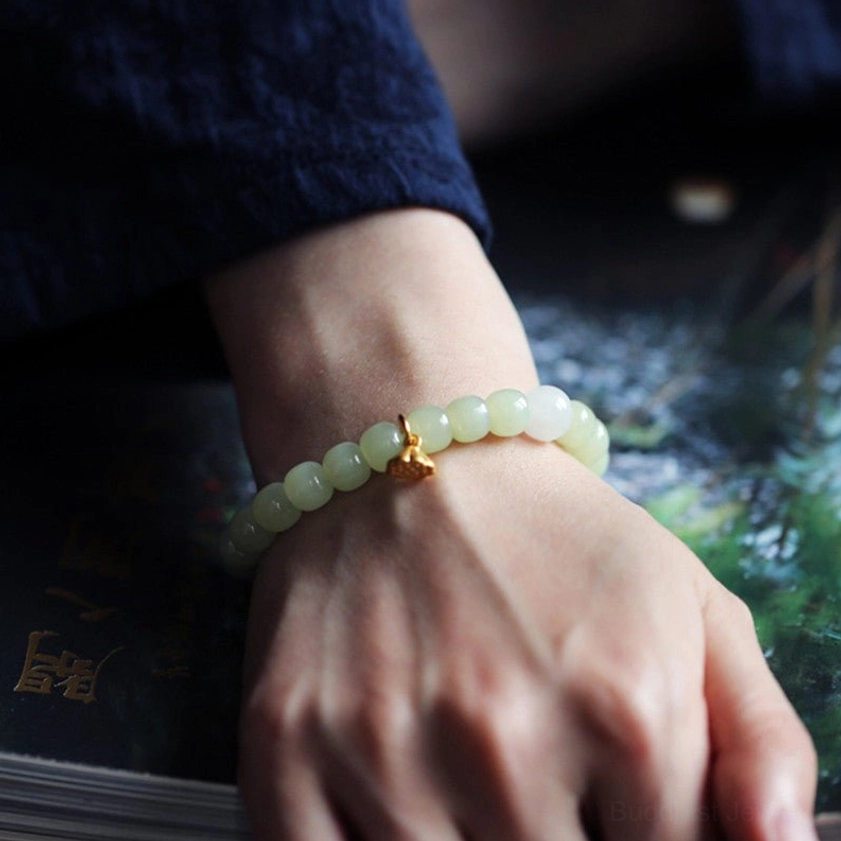 Smooth green jade beads with gold lotus charm, side view on wrist showing neat strand