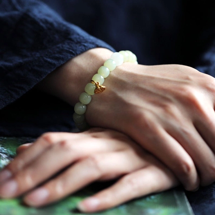 Adjustable jade bracelet with lotus charm worn on wrist, paired hands showing natural color