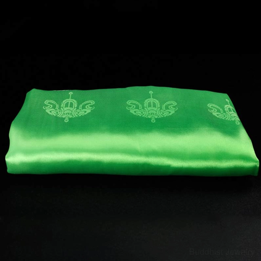 Single green khata scarf flat overhead view on black background showing emerald green satin with embossed light green decorative patterns