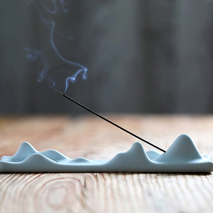 Green ceramic mountain peak incense holder on wooden surface with rising incense smoke