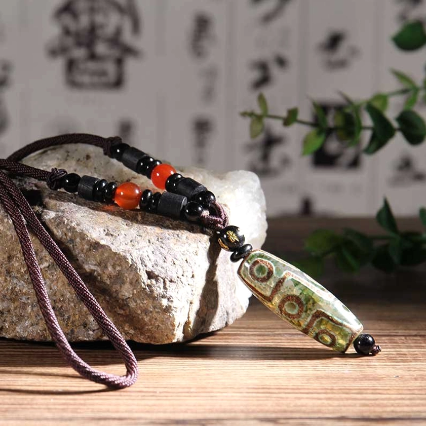 Green patterned nine-eye dzi bead necklace with brown rope and black-red spacer beads on wooden surface