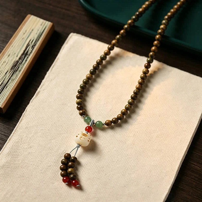 Green sandalwood beaded mala bracelet with variegated wood tones and carved cat tassel on dark linen paper