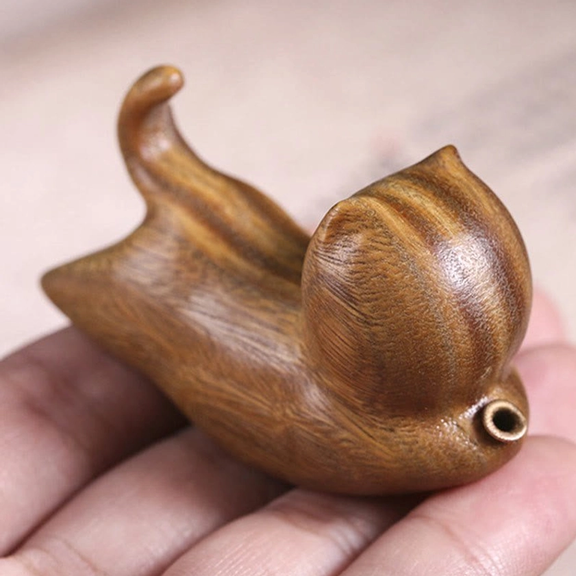 Green sandalwood cat incense holder held in human hand, demonstrating compact size and natural wood grain texture with metal incense socket
