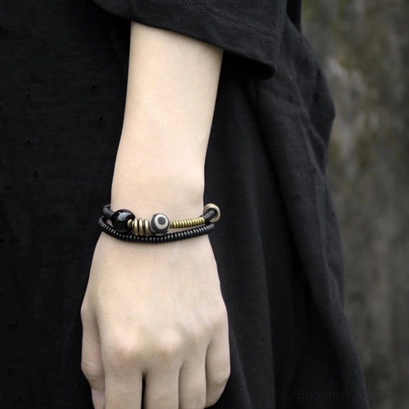 Green sandalwood brass dzi bead bracelet fitted neatly on wrist dark fabric background