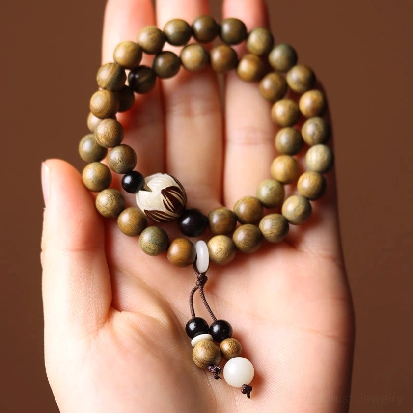 Hand holding green sandalwood lotus bracelet showing double wrap design, central carved lotus bead and decorative tassel pendant
