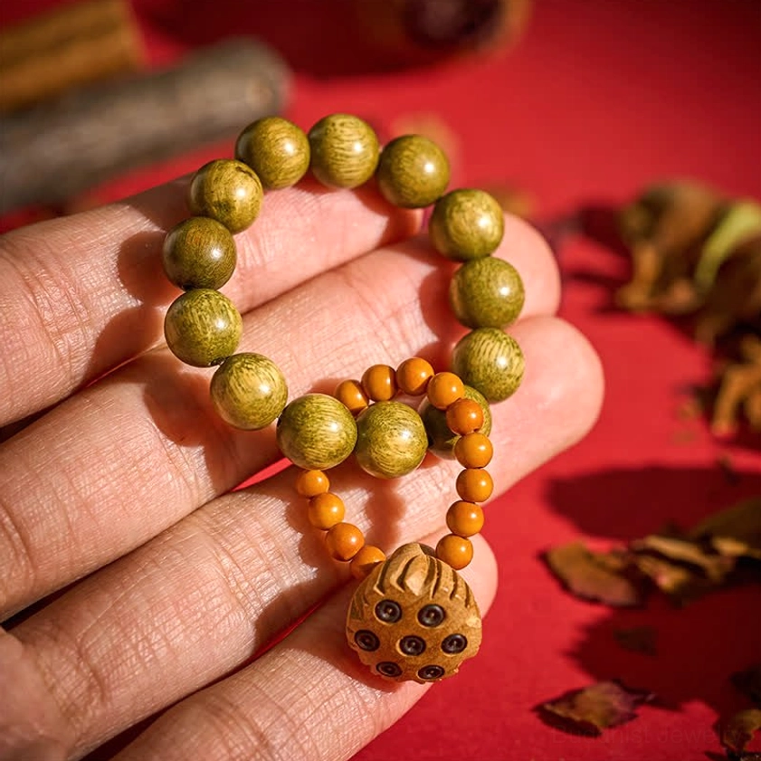 Green sandalwood meditation palm beads with carved lotus pod charm, hand-held close-up view showing polished wooden beads and orange spacer accents