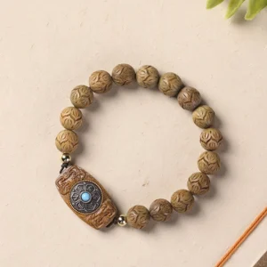 Green sandalwood Om Mani Padme Hum carved wooden bracelet with turquoise charm, flat lay on beige background