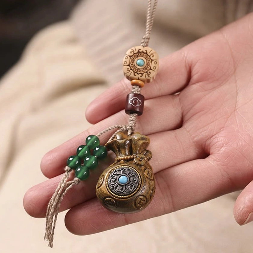 Green sandalwood Om Mani Padme Hum phone charm held in palm showing carved Tibetan beads and blue metal inlay
