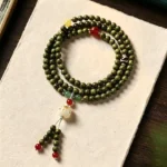 Green sandalwood Buddhist prayer mala bracelet with cat charm tassel, overhead flat lay view showcasing natural wood beads