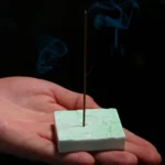 Handcrafted green ceramic square cloud incense burner with embossed Buddhist cloud pattern held in palm, showing glossy glaze finish and burning incense with rising smoke
