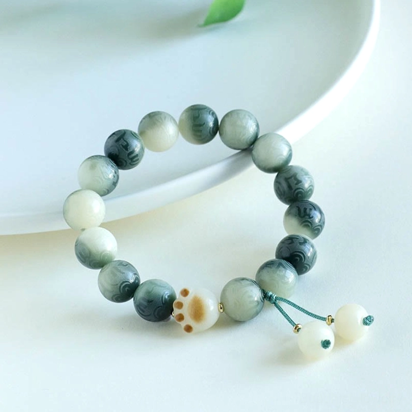 Green and white Bodhi Seed bracelet featuring mixed natural seed beads with carved mantra and decorative tassel accents
