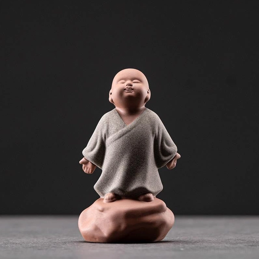 Grey ceramic looking up monk figurine in contemplative stance on stone-shaped base, studio frontal shot