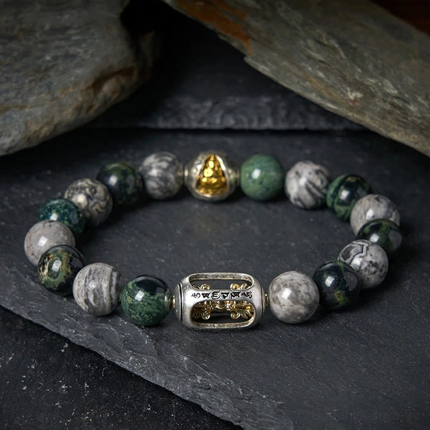 Grey Jasper Buddhist healing bracelet with Om Mani Padme Hum engraved charm and gold Buddha bead, top-down flat lay on dark stone