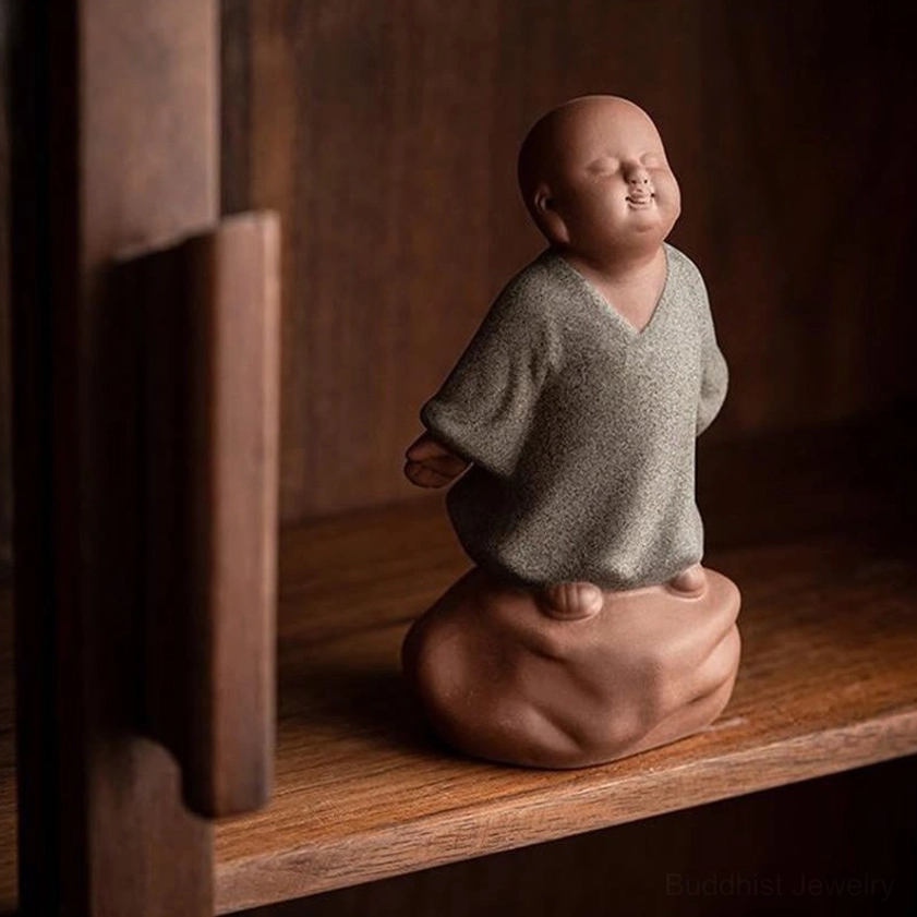 Grey ceramic monk statue displayed on vintage wooden shelf with spiritual decor side view