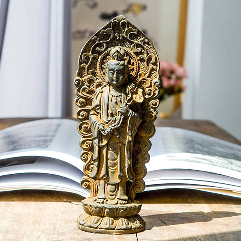 Standing Guanyin bodhisattva Buddha statue holding sacred ruyi scepter with ornate halo carvings, handcrafted iron powder resin sculpture on wooden table with spiritual book